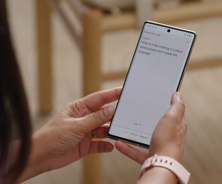 A person wearing a watch with a pink band holds a Google Pixel phone and looks at a translation.