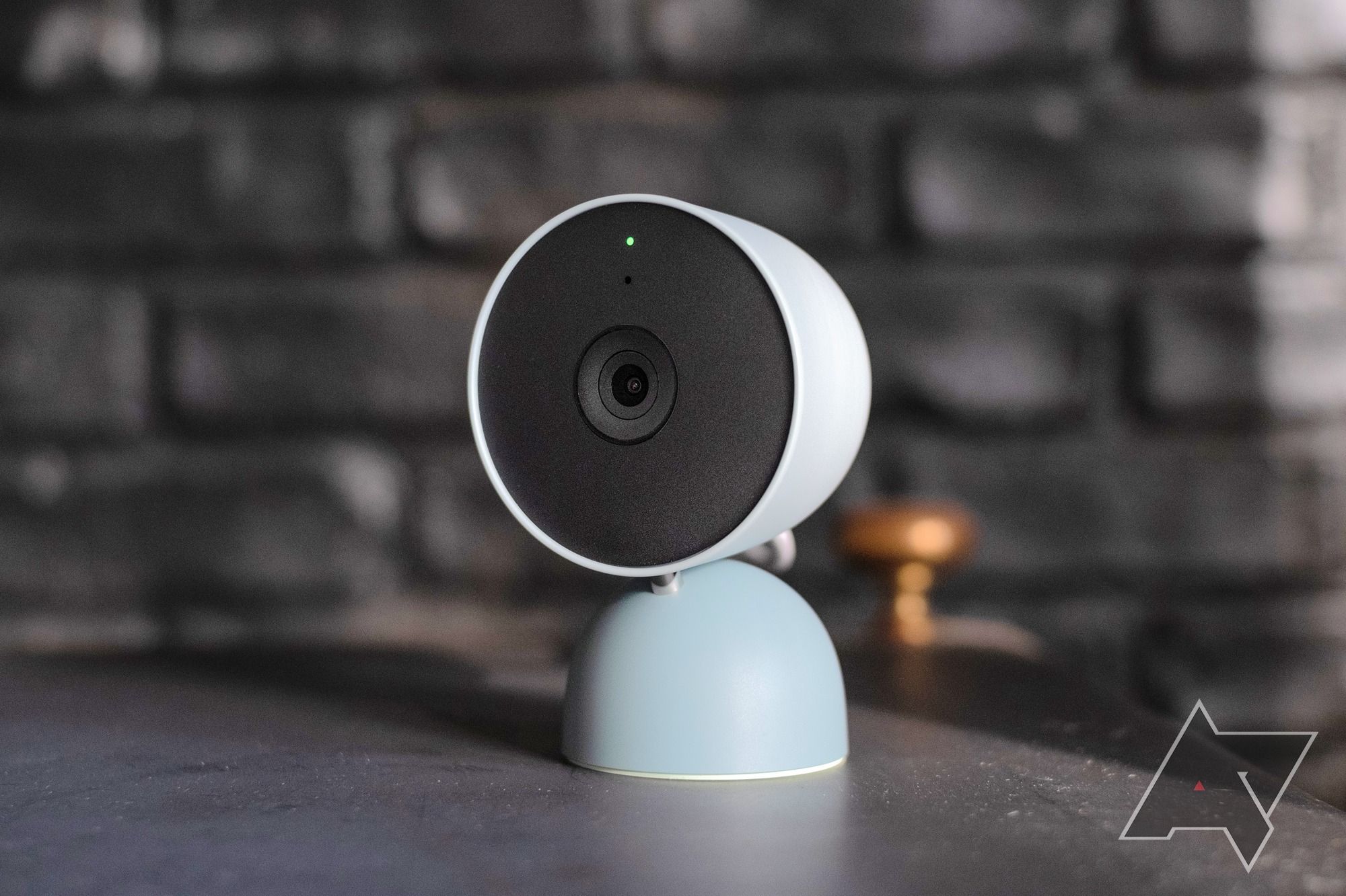 A blue Google Nest camera in front of a black brick background.