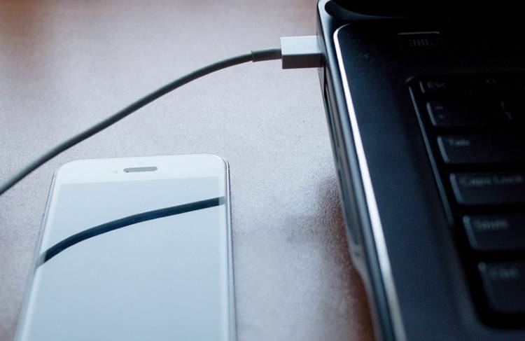 A USB cable coming from a computer to the right of the phone it is plugged into