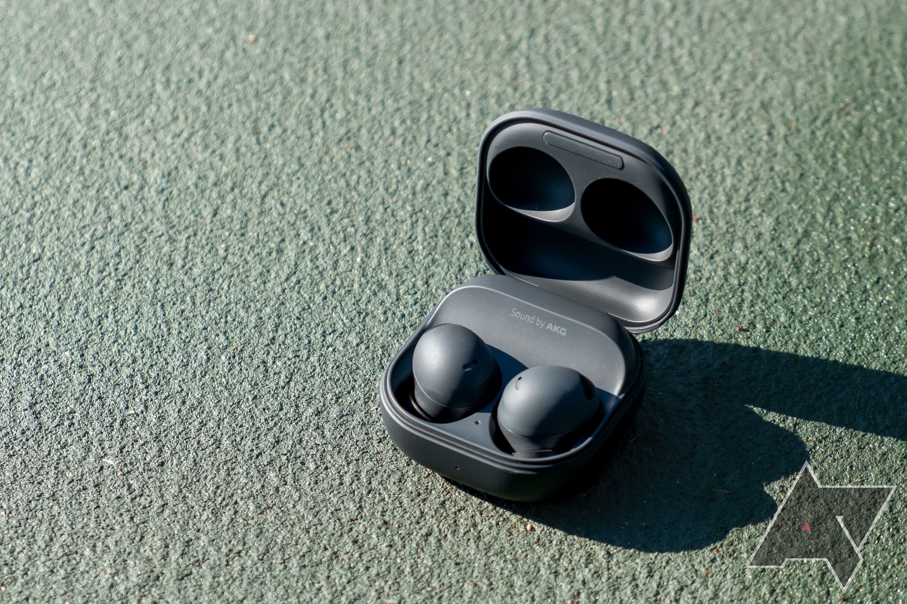 The Samsung Galaxy Buds 2 Pro in their case with the lid open on a green background, with a sharp shadow to the right
