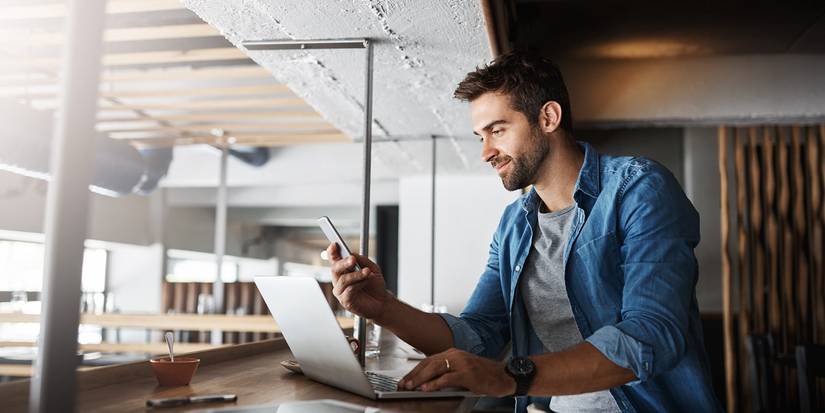 Man Smiling at Phone While Working on Laptop