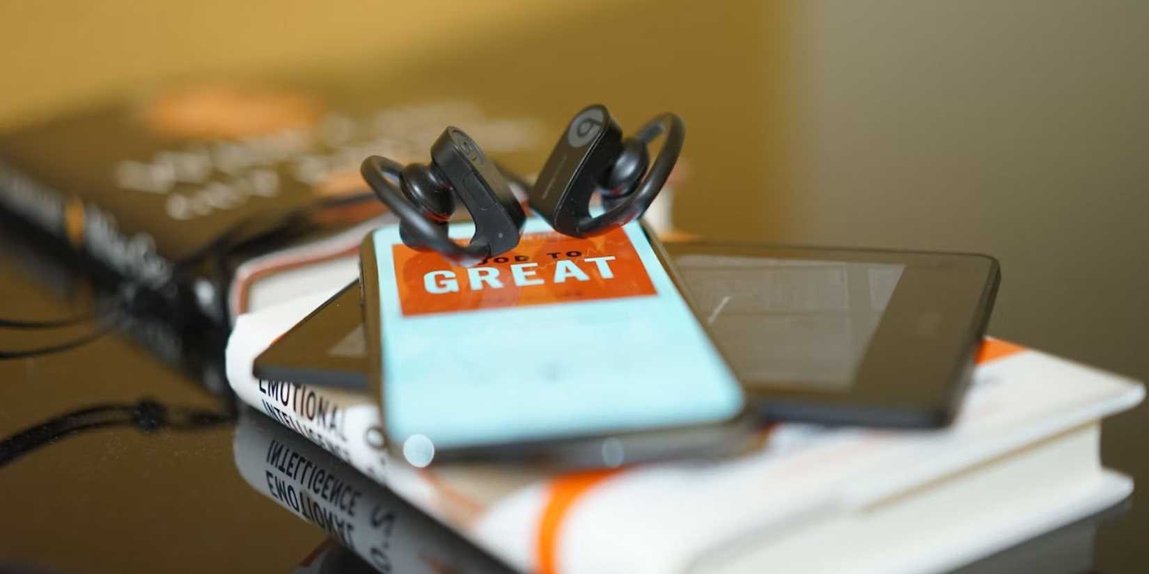 two black earbuds resting on a phone that's on a kindle that's on a book that's on a table