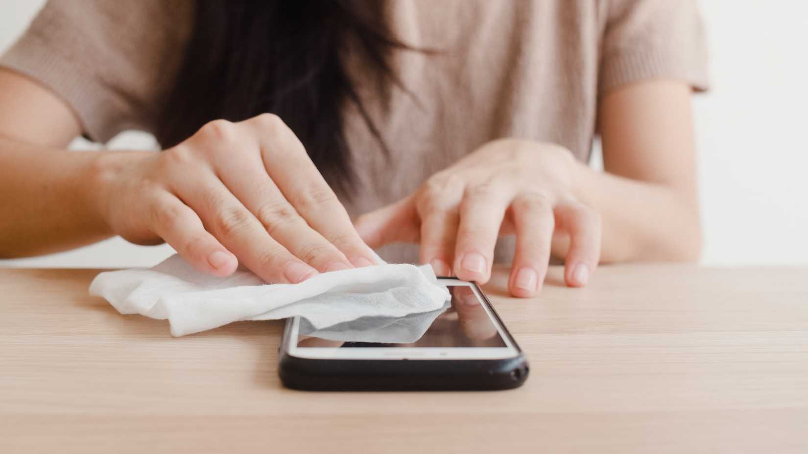 uma mulher limpando suavemente toda a tela do telefone com um pano de microfibra