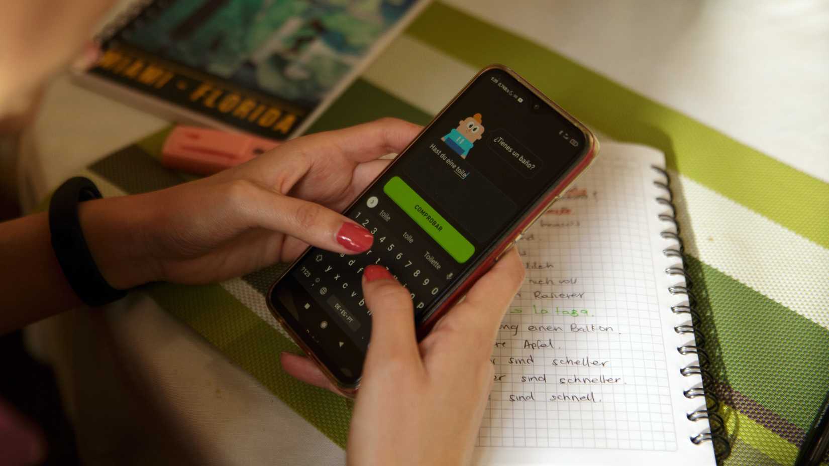 A person using Duolingo on a phone with a notebook in the background
