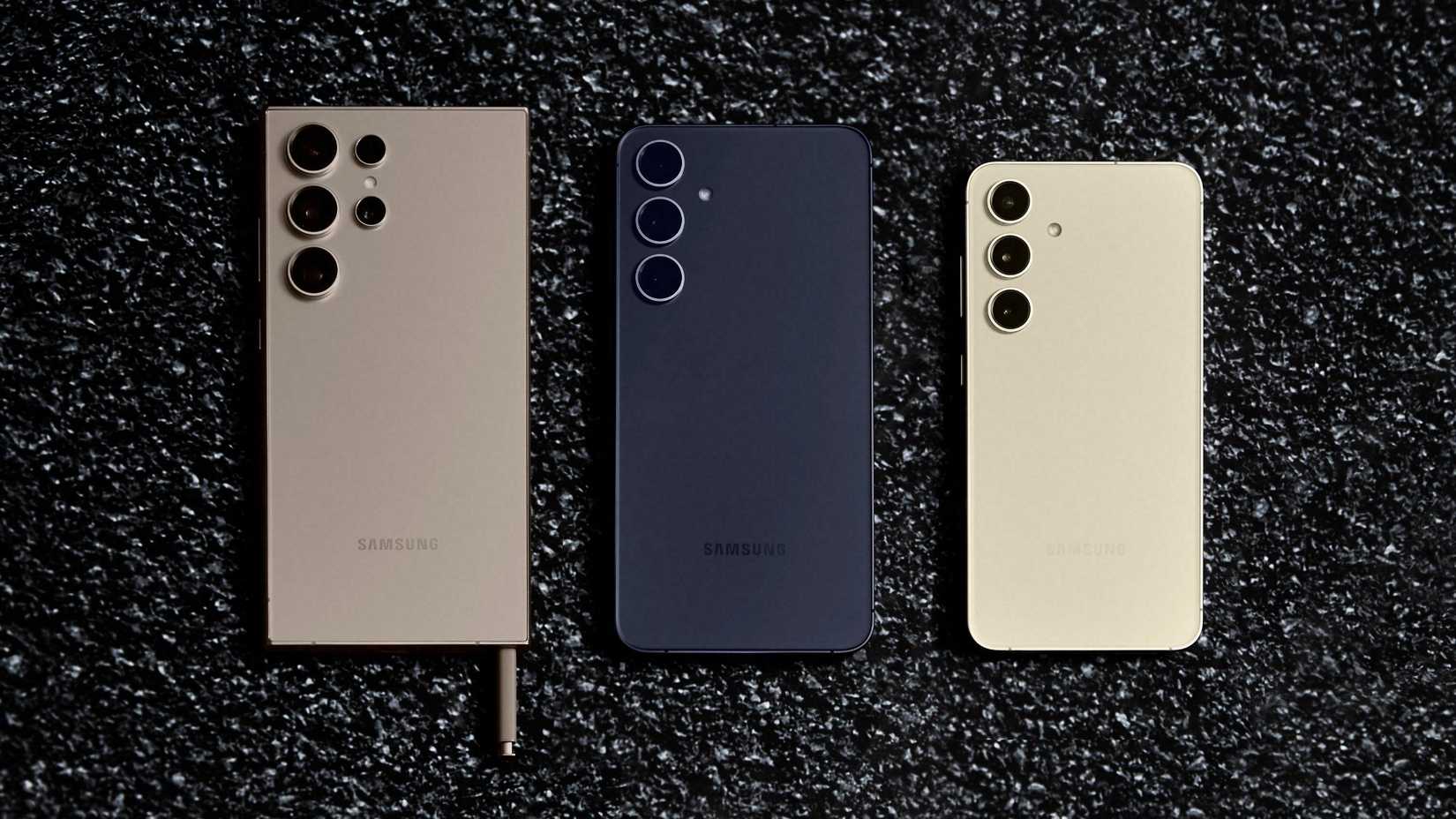 A Titanium Gray S24 Ultra, Cobalt Violet Galaxy S24+, and Amber Yellow S24 lying flat on a speckled black surface