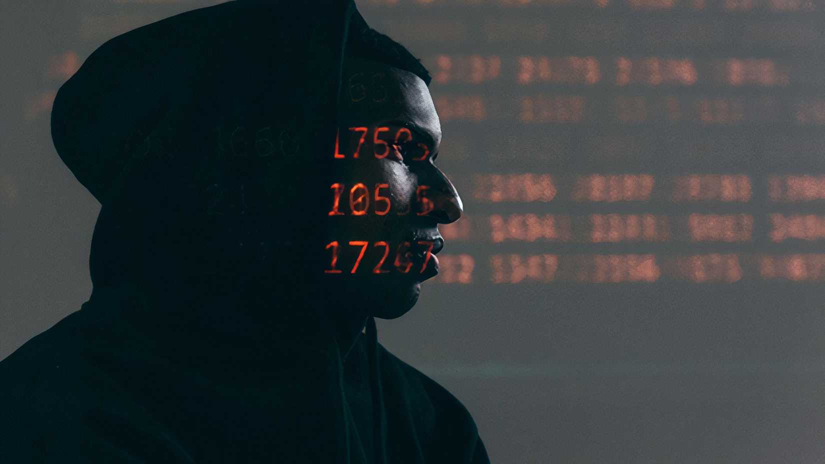 A hacker in a blackhood looking at something