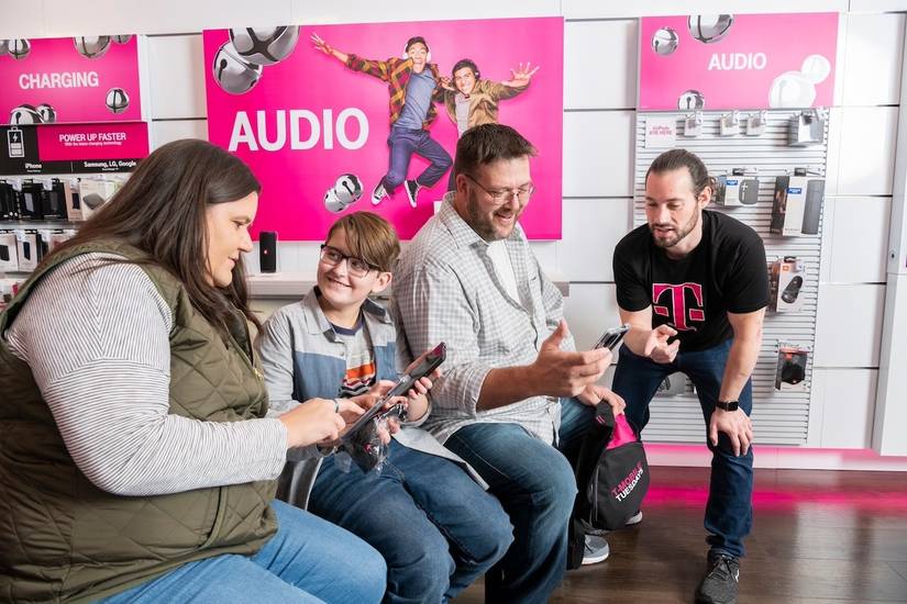 Parents and child holding phones and talking with T-Mobile store representative