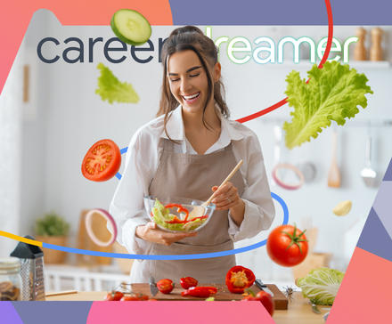 Smiling woman in a kitchen preparing a fresh salad with floating vegetables around her.