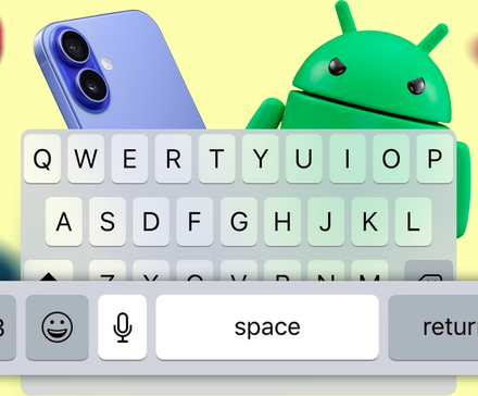 An angry Android mascot peeks over an iPhone keyboard