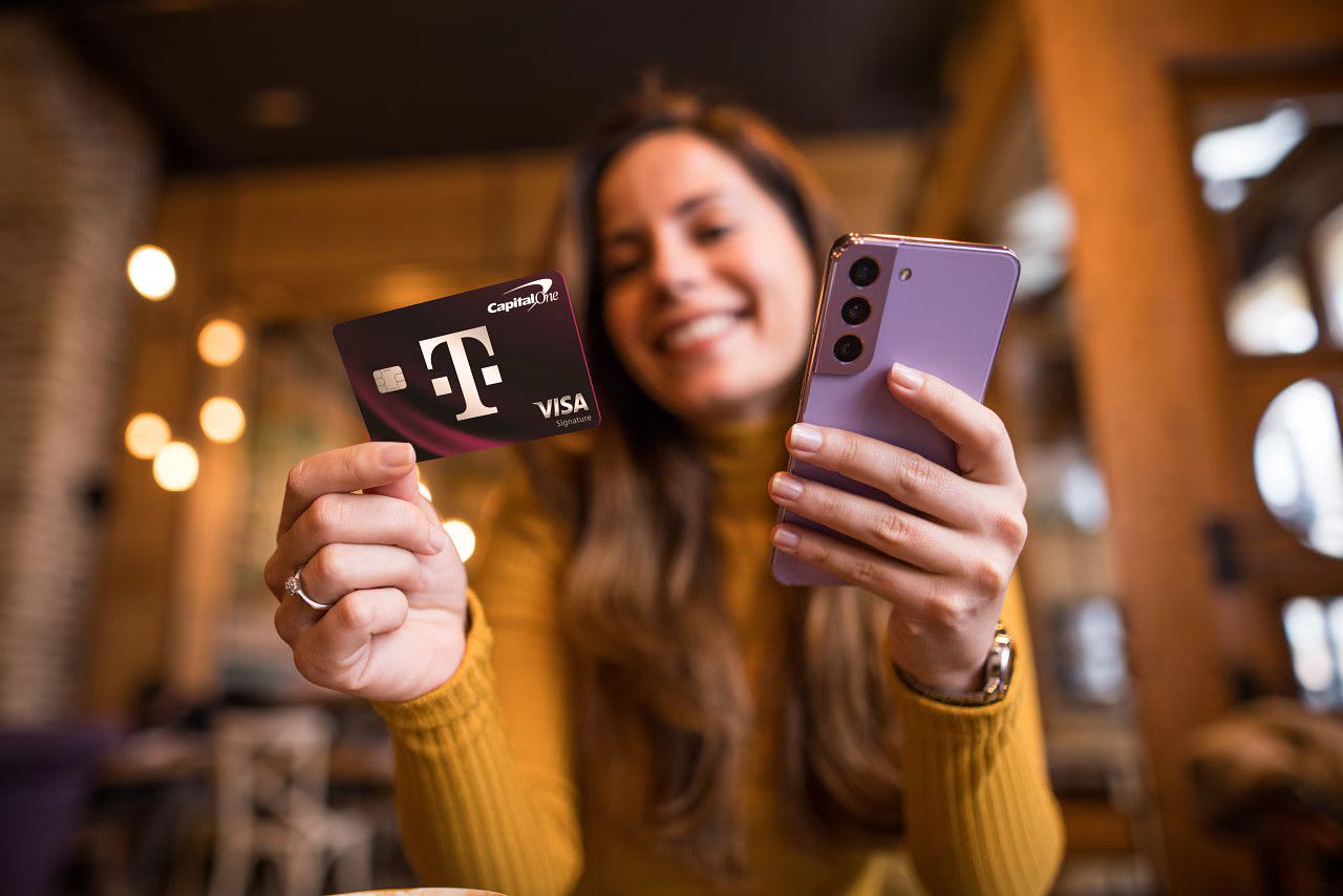 The T-Mobile and Capital One credit card being held by a woman with her smartphone in her other hand. She seems oddly happy with her credit card.
