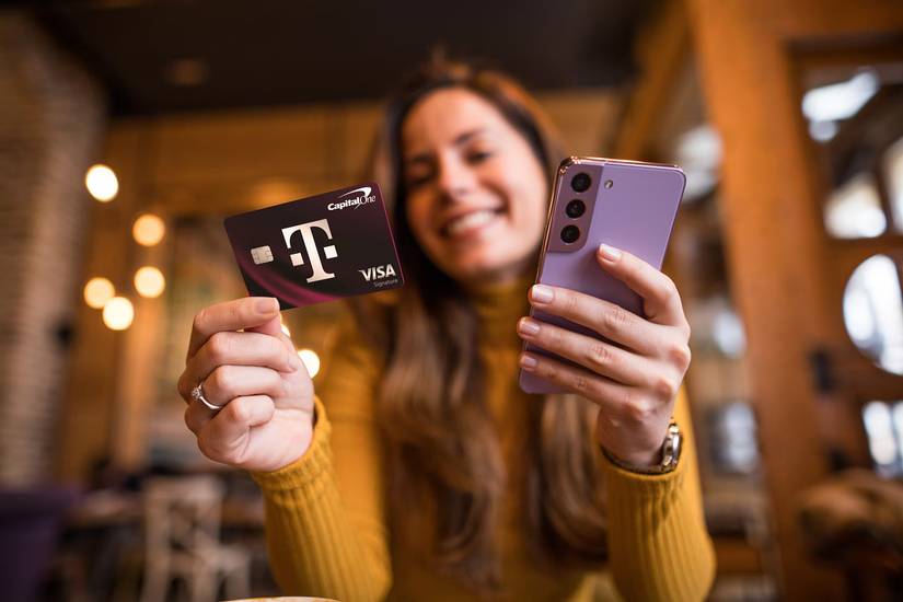 La carta di credito T-Mobile e Capital One tenuta da una donna con il suo smartphone nell'altra mano. Sembra stranamente soddisfatta della sua carta di credito.