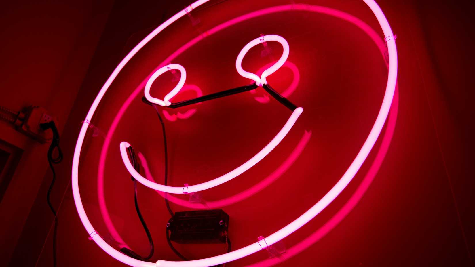 uma foto de um rosto sorridente iluminado por néon vermelho na parede