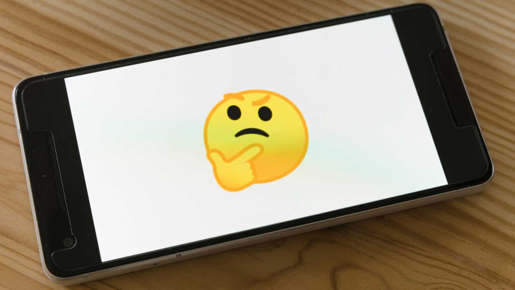 uma foto de um smartphone sobre uma mesa de madeira exibindo um emoji intrigante sobre um fundo branco