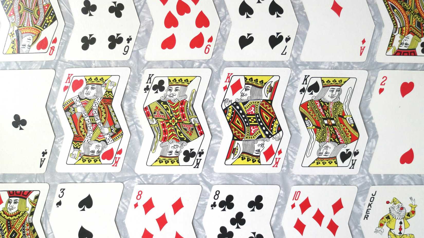 una foto di diverse file di carte da gioco tagliate in forma ondulata, con tutti e quattro i semi dei re al centro