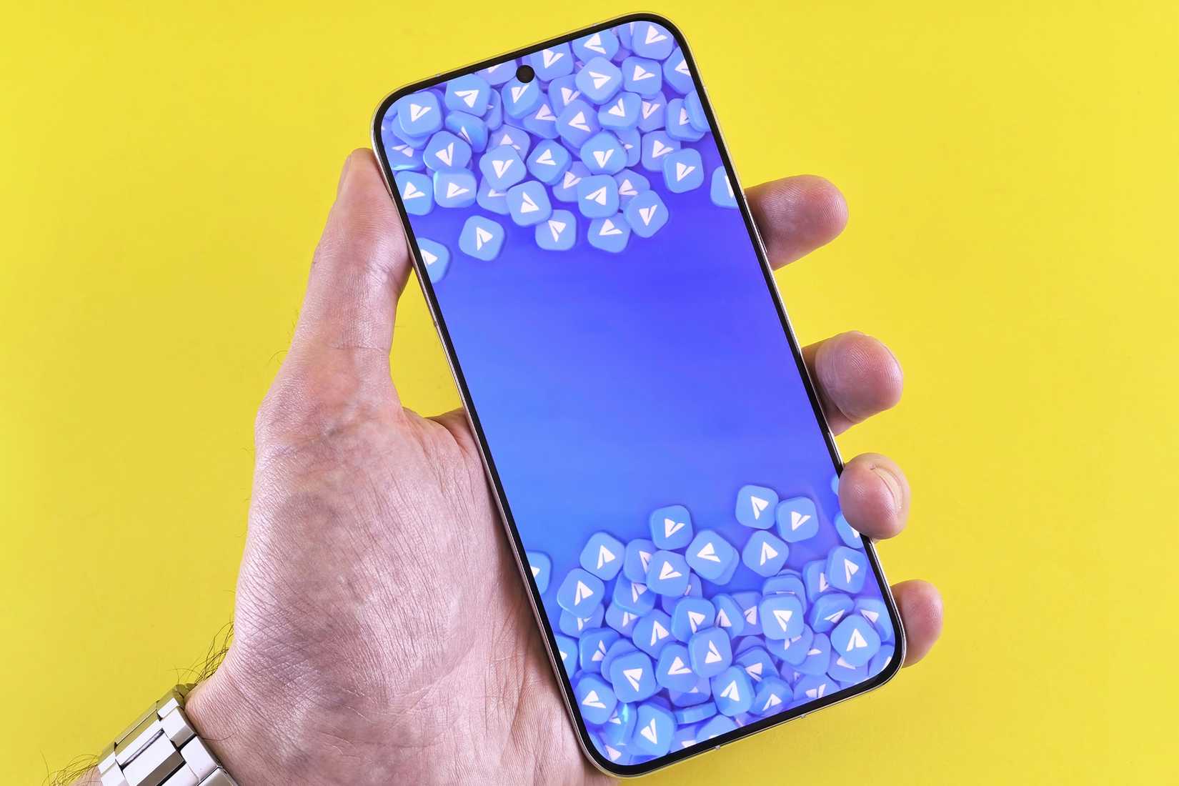 una mano che tiene uno smartphone su cui sono visualizzate molte icone di posta elettronica, su uno sfondo giallo