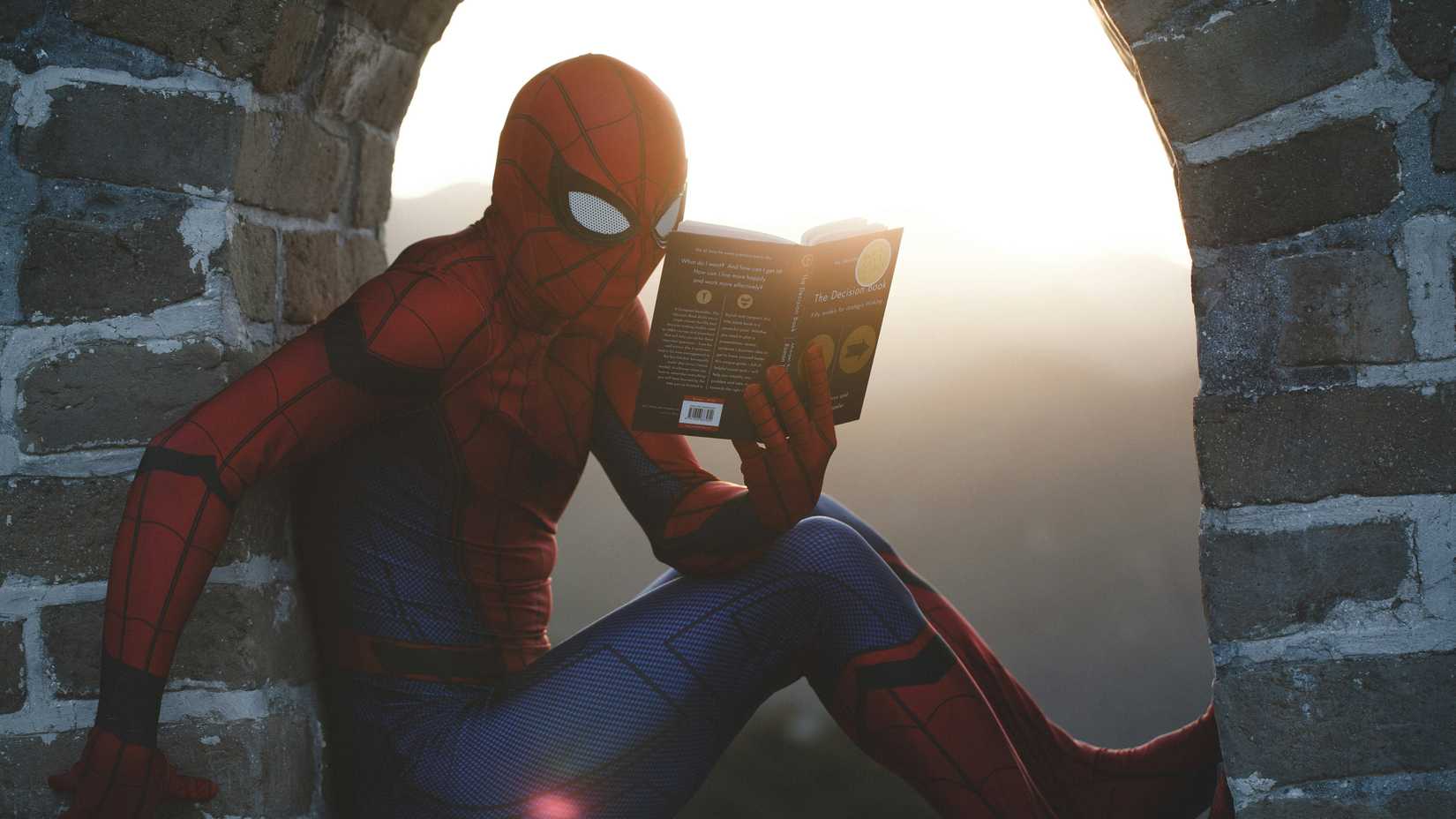 Una foto di Spiderman seduto alla finestra, mentre legge un libro