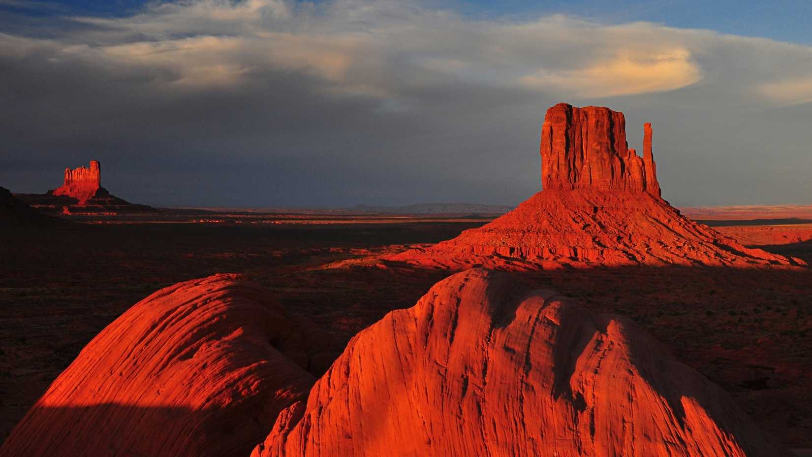 Uma imagem de um deserto com rochas avermelhadas e nuvens no céu