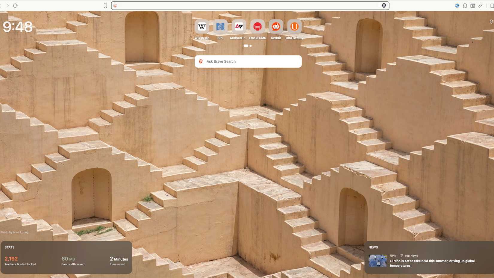 Uma captura de tela do Brave Browswer com uma nova guia aberta mostrando uma foto de fundo com uma série de degraus sobre portas em edifícios cor de areia e a barra de pesquisa do Brave no topo da foto