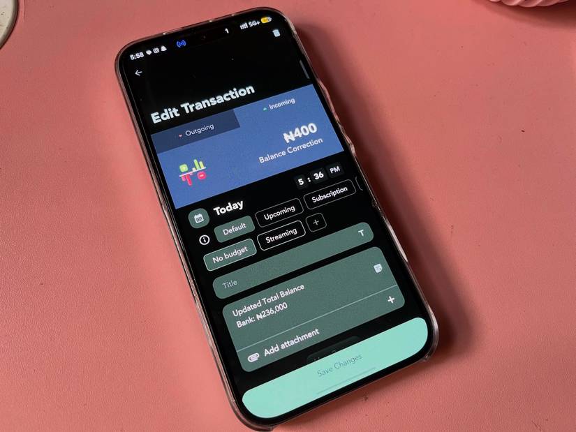 Telefono su tavolo rosa che mostra l'app finanziaria e i campi di immissione per la modifica delle spese