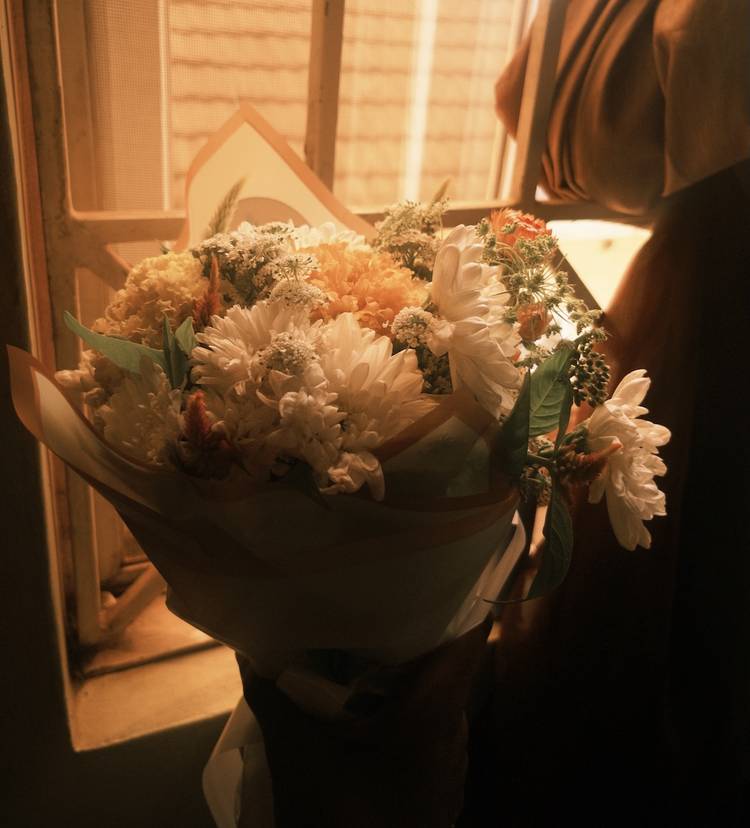 Hand holding fresh flower bouquet beside window