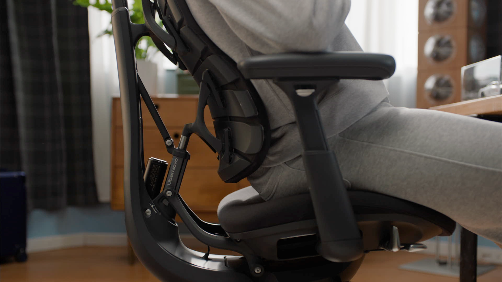 A person in a grey sweatsuit leans into the lumbar support of a black ergonomic chair.