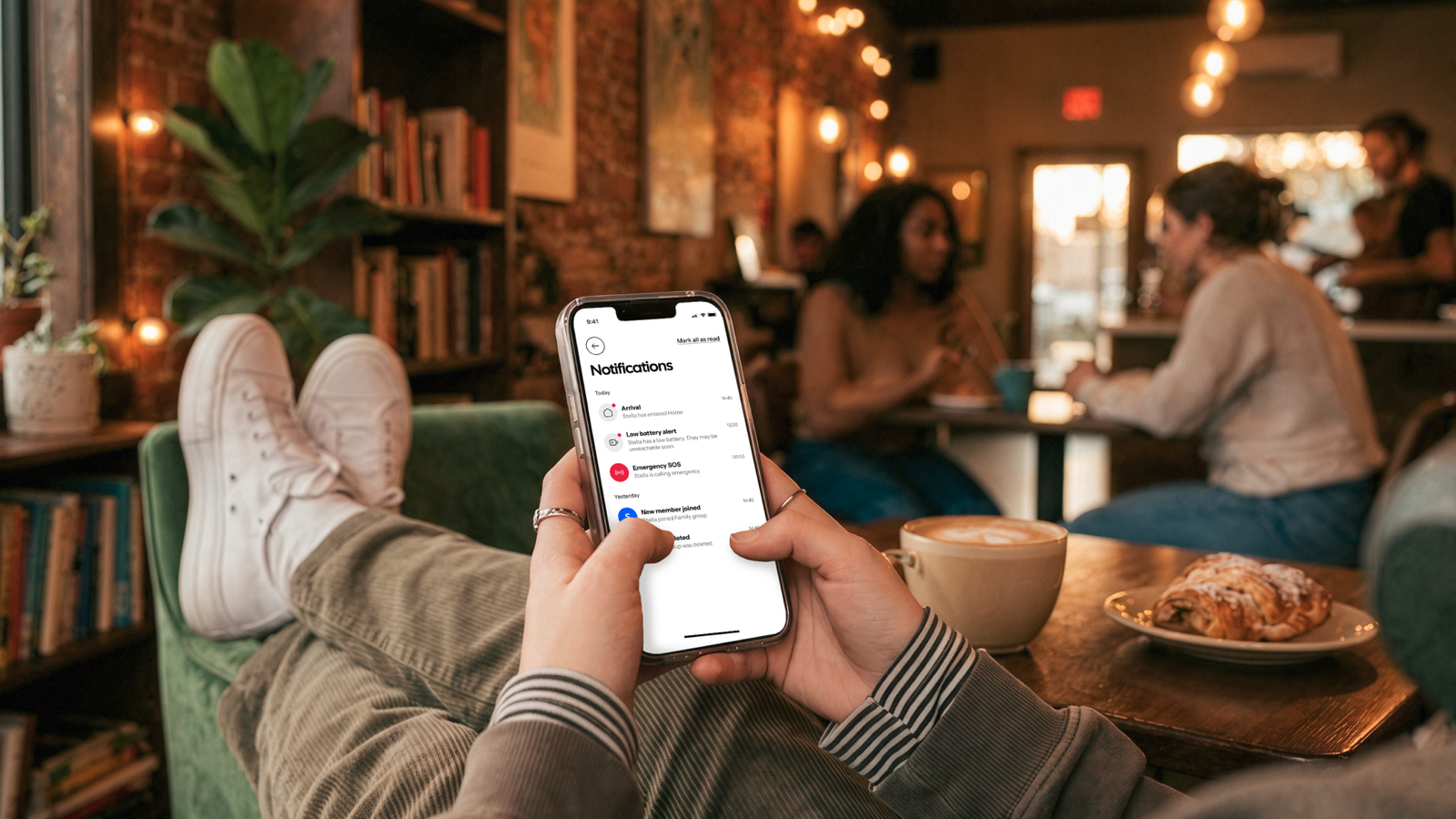 A person sitting with their feet up small cafe while holding a smartphone displaying the notifications screen of the HeyPolo app.