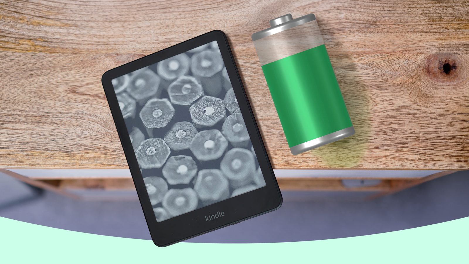 Kindle e-reader beside a battery icon on a wooden table.