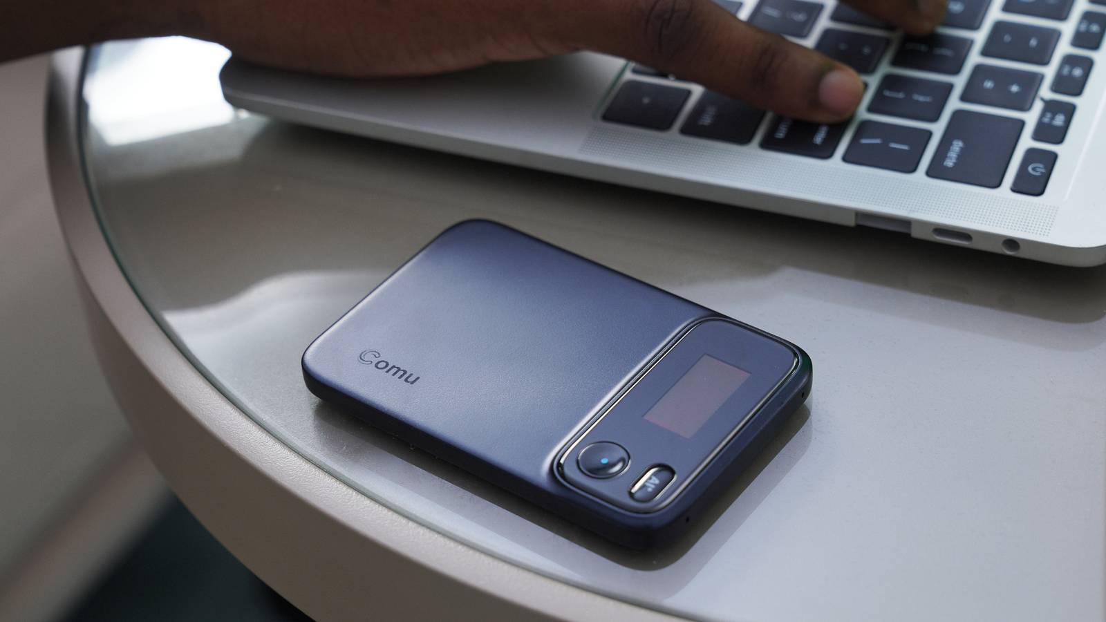 The Comu Action Pro sitting on a table next to someone's laptop.