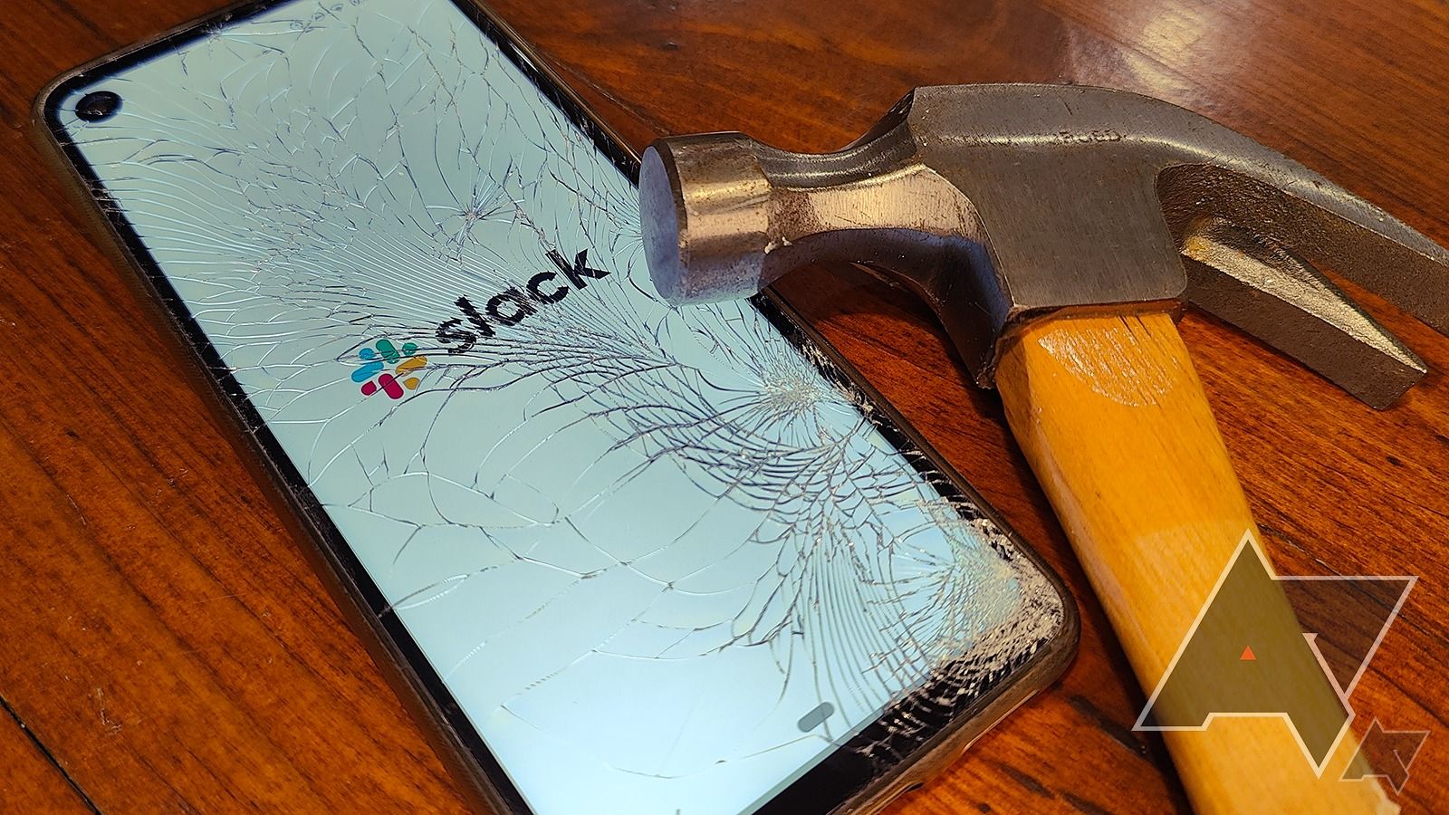 Ponsel cerdas menampilkan logo Slack melalui layar yang retak sementara palu diletakkan di layar