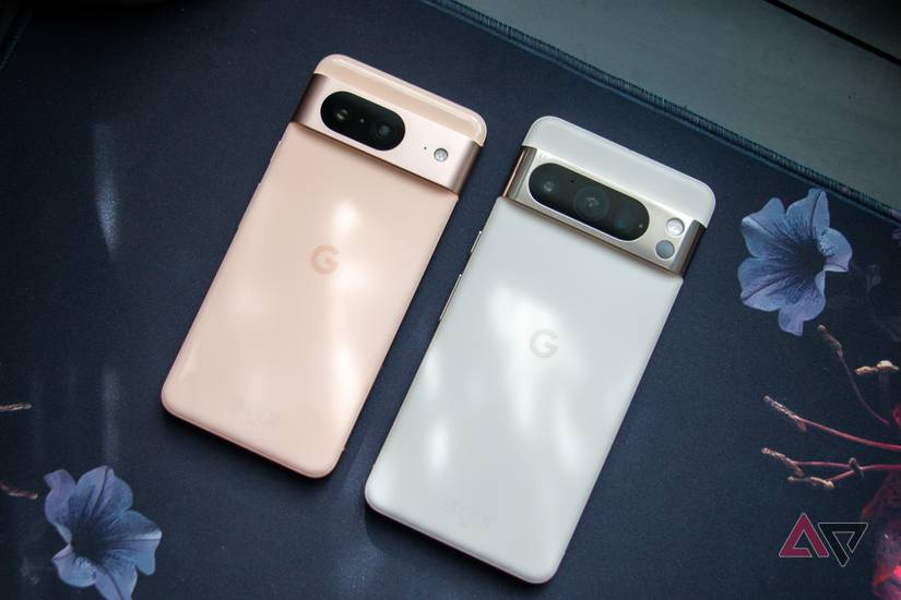 The Google Pixel 8 and Pixel 8 Pro laying next to each other on a desk mat, with sunlight gently hitting the backs of both devices.