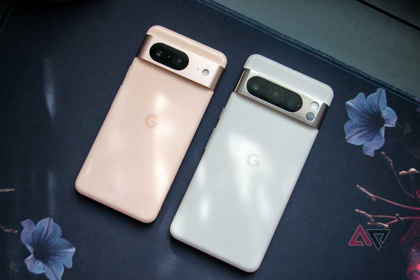 The Google Pixel 8 and Pixel 8 Pro laying next to each other on a desk mat, with sunlight gently hitting the backs of both devices.