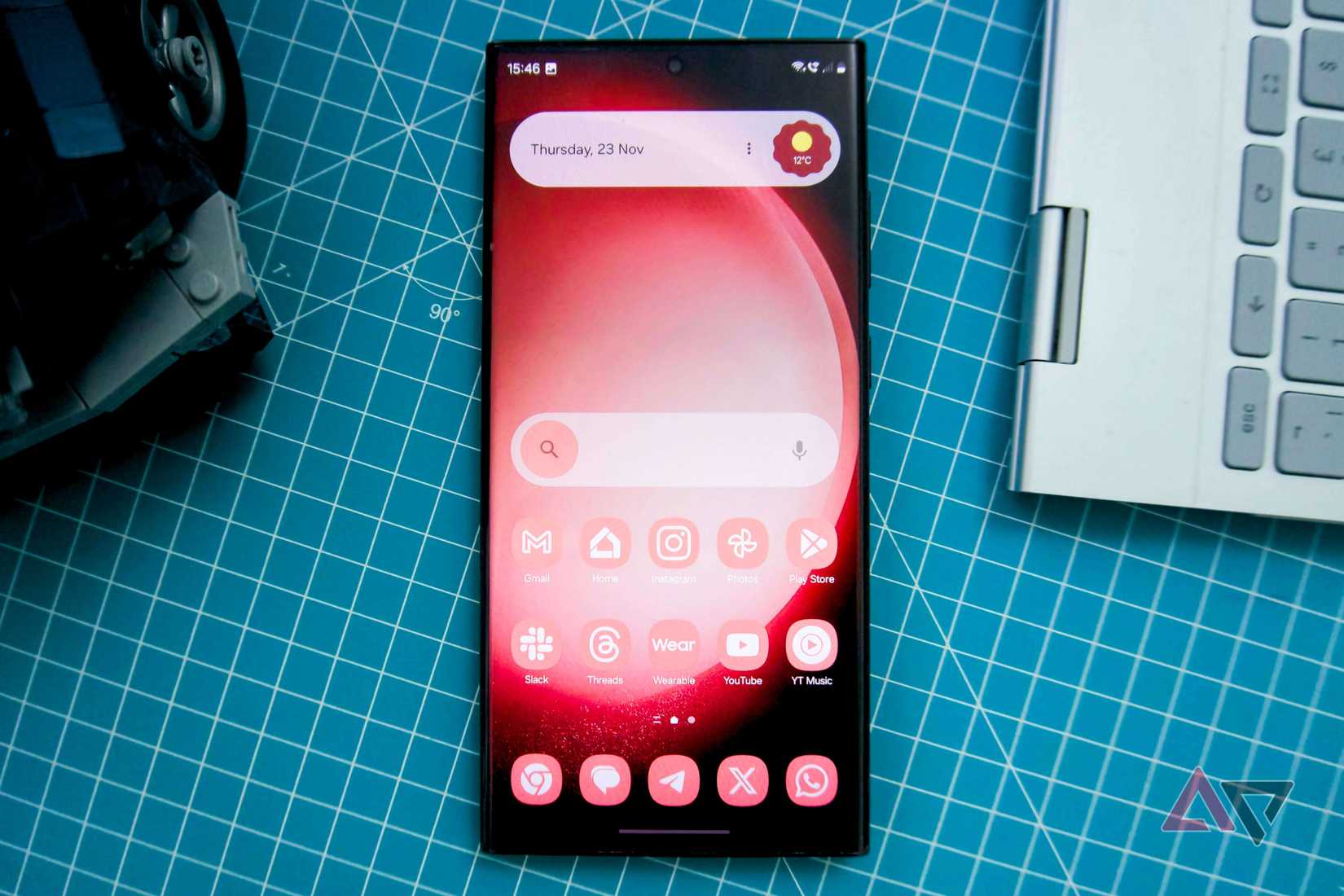 Una foto di un Galaxy S23 Ultra con un widget di ricerca Google personalizzato su uno sfondo a griglia blu e bianco, con un'auto Lego e una tastiera 