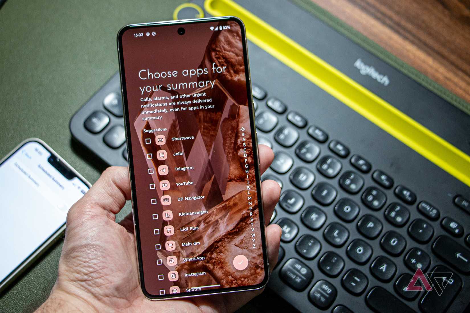 Um Google Pixel 8 Pro na mão, executando a tela de configuração do Niagara Launcher para resumo de notificação, com um teclado e um iPhone 13 visíveis em segundo plano