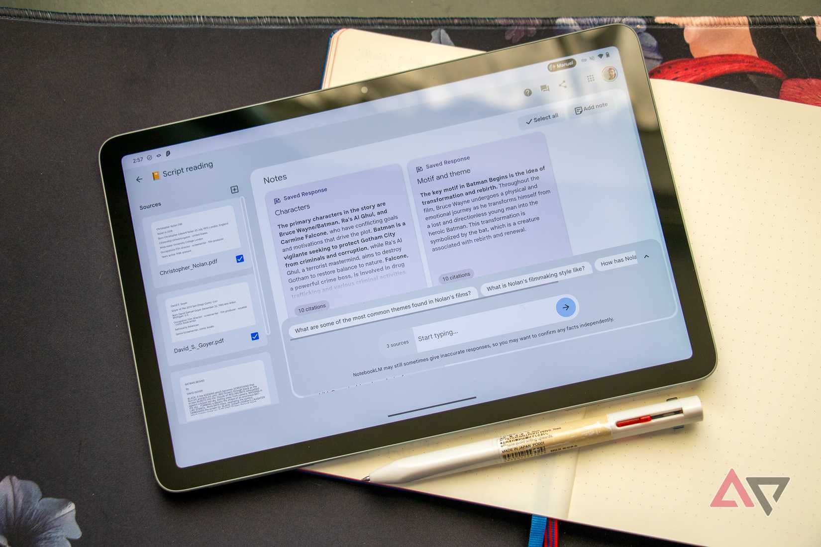A tablet with NotebookLM website opened laying on a table with a physical notebook beneath it
