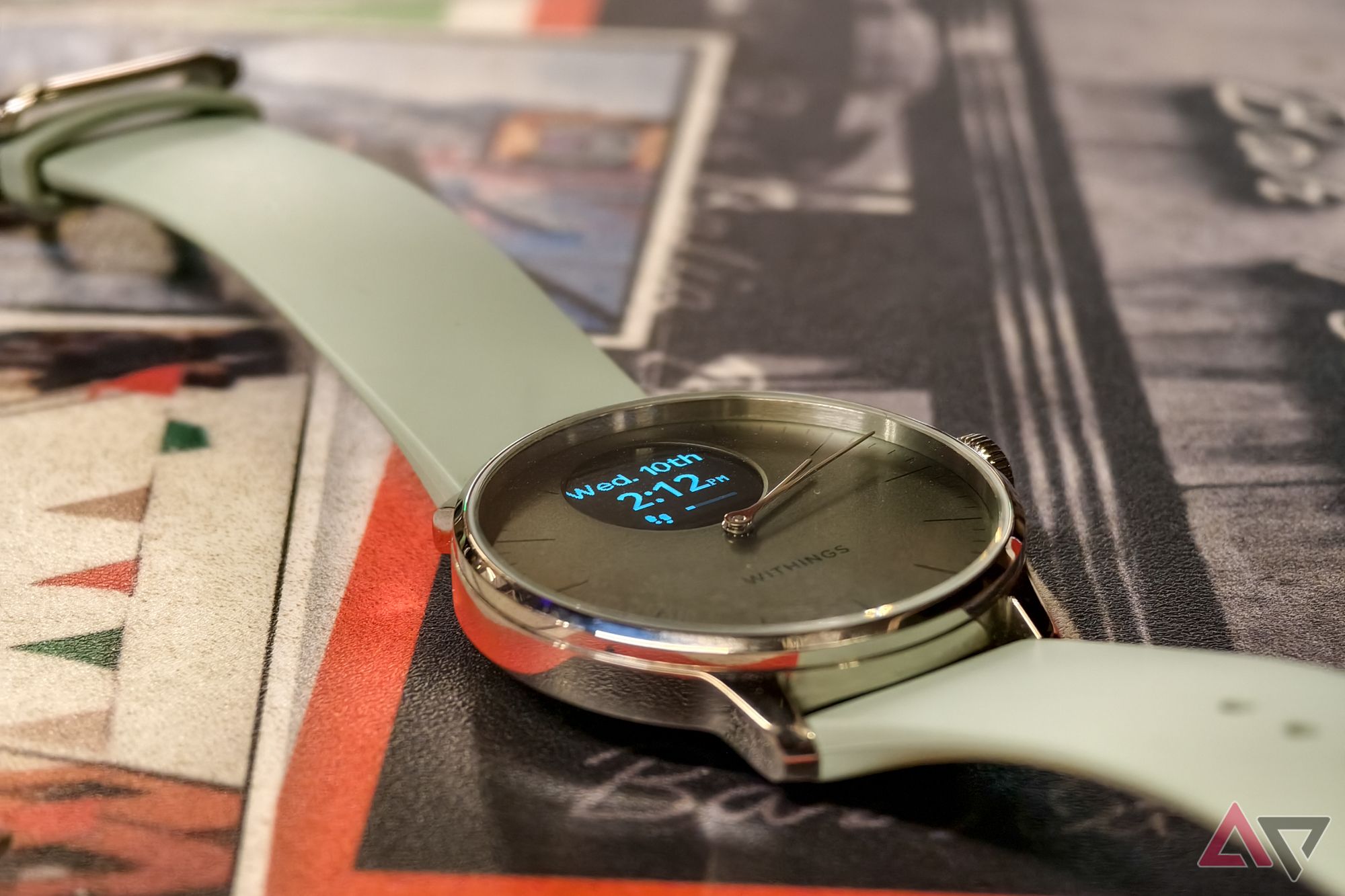 Withings ScanWatch Light in Green, with the display on, photographed from above at an angle with a close-up on the watch face, resting on an Italian restaurant table