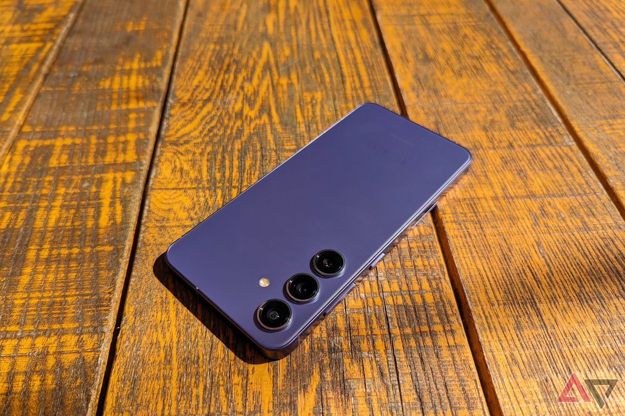 The Samsung Galaxy S24 upside down on a sunny wooden table in Cobalt Violet