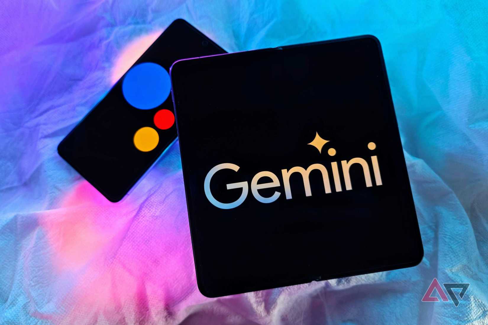 OnePlus aberto com o logotipo do Google Gemini e o Pixel 8 Pro com o logotipo do Google Assistant em uma tabela com luzes RGB