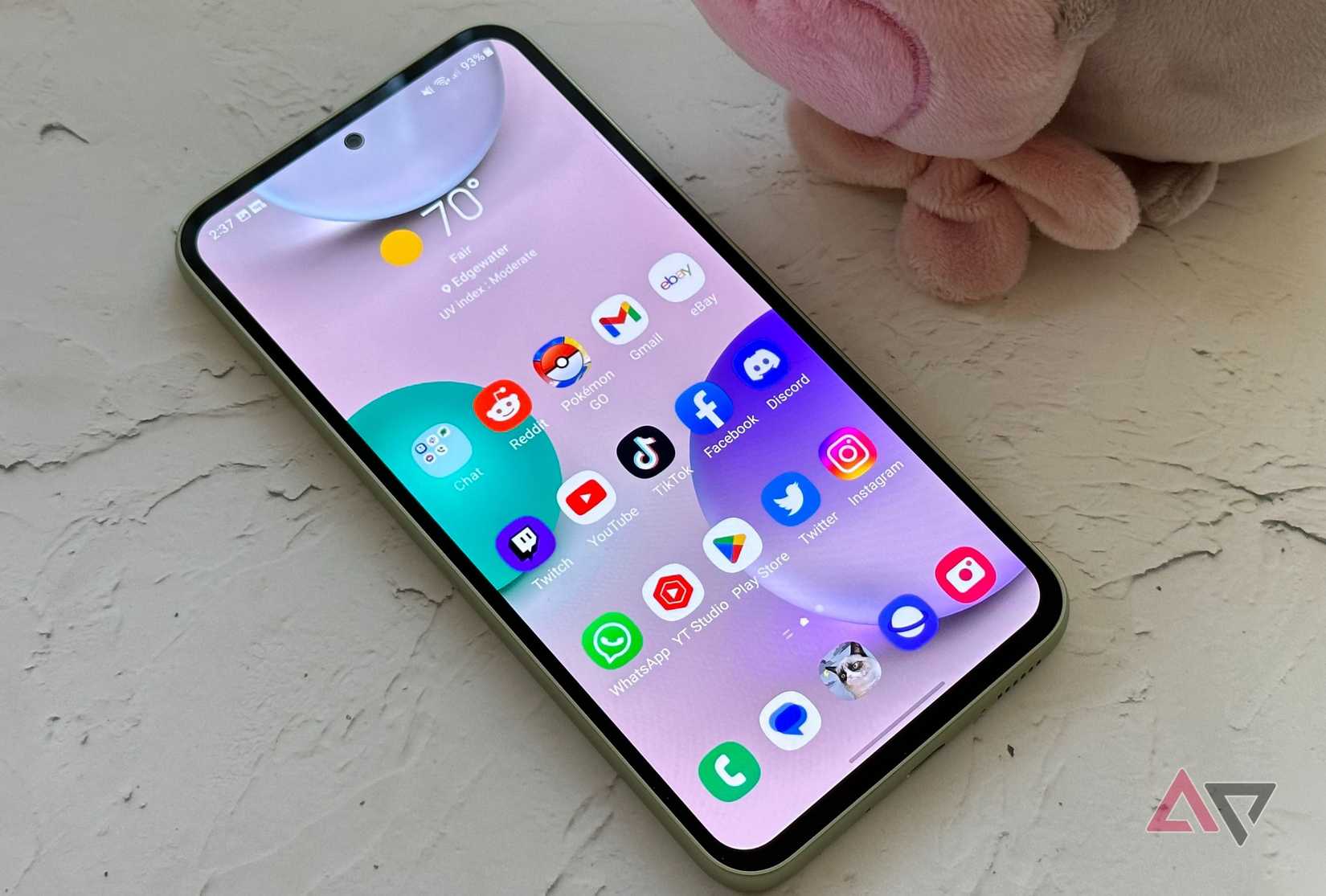 O Samsung Galaxy A54 5G em uma mesa com um pelúcia ao lado