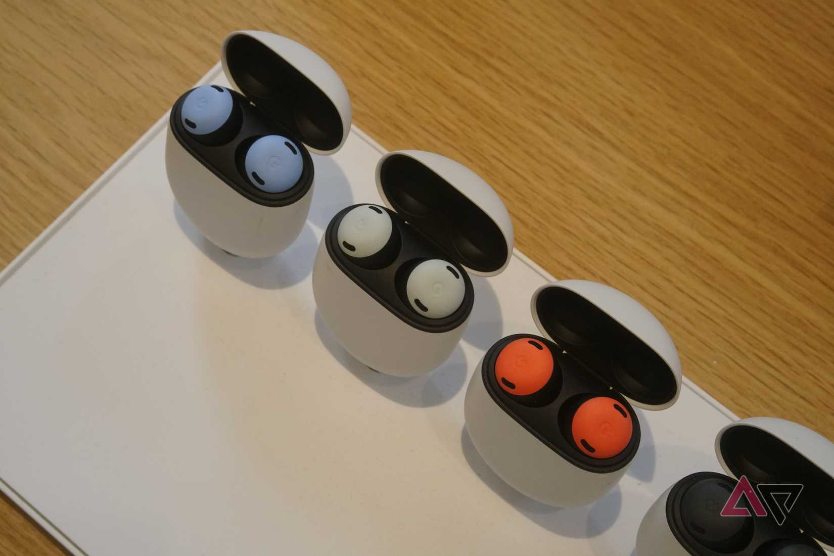 Three pairs of Pixel Buds Pro in blue, white, and red colors laid out in their charging cases.