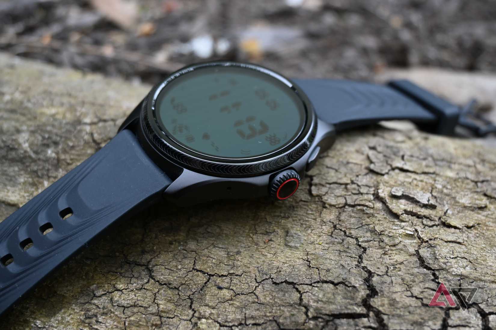 Mobvoi TicWatch Pro 5 Enduro mostrando seu lado direito e a tela deitado sobre um tronco.