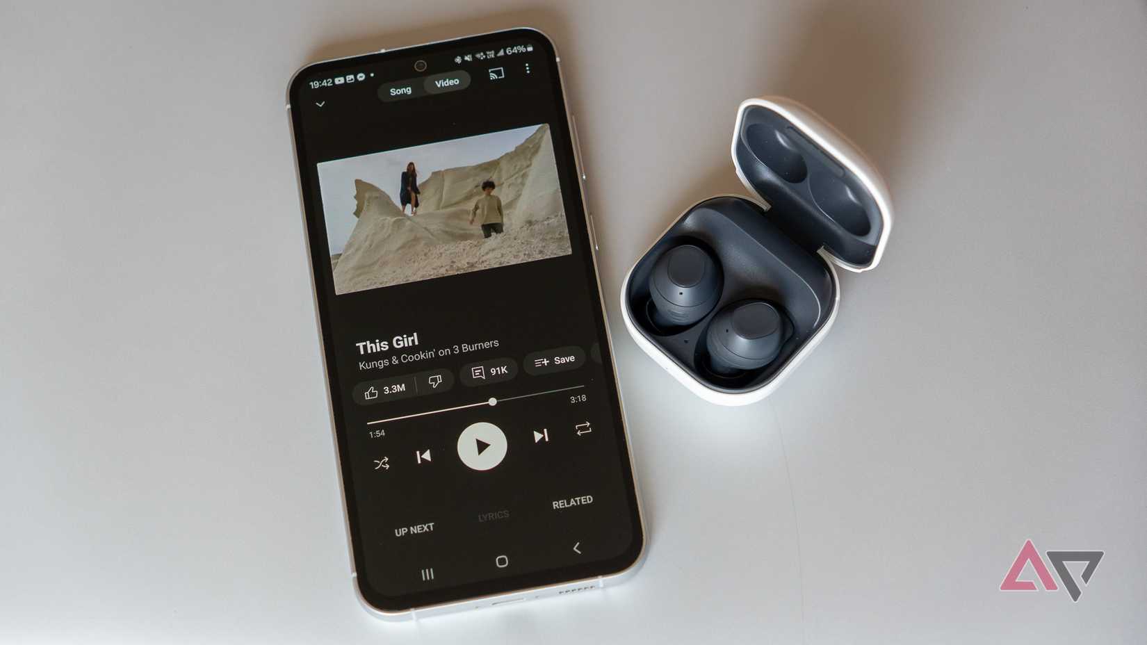 YouTube Music Premium reproduzido em um telefone Samsung próximo aos fones de ouvido sem fio Samsung em uma superfície de metal cinza.