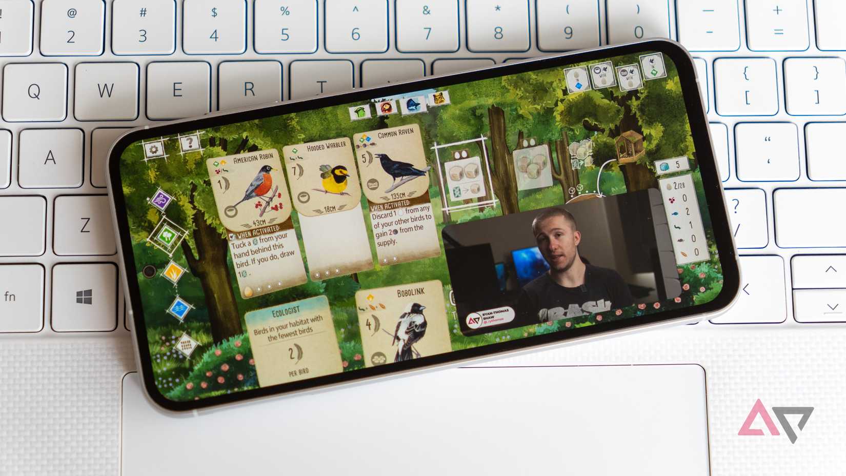 Um jogo e um vídeo sendo reproduzidos simultaneamente em um telefone Samsung em um teclado de laptop branco