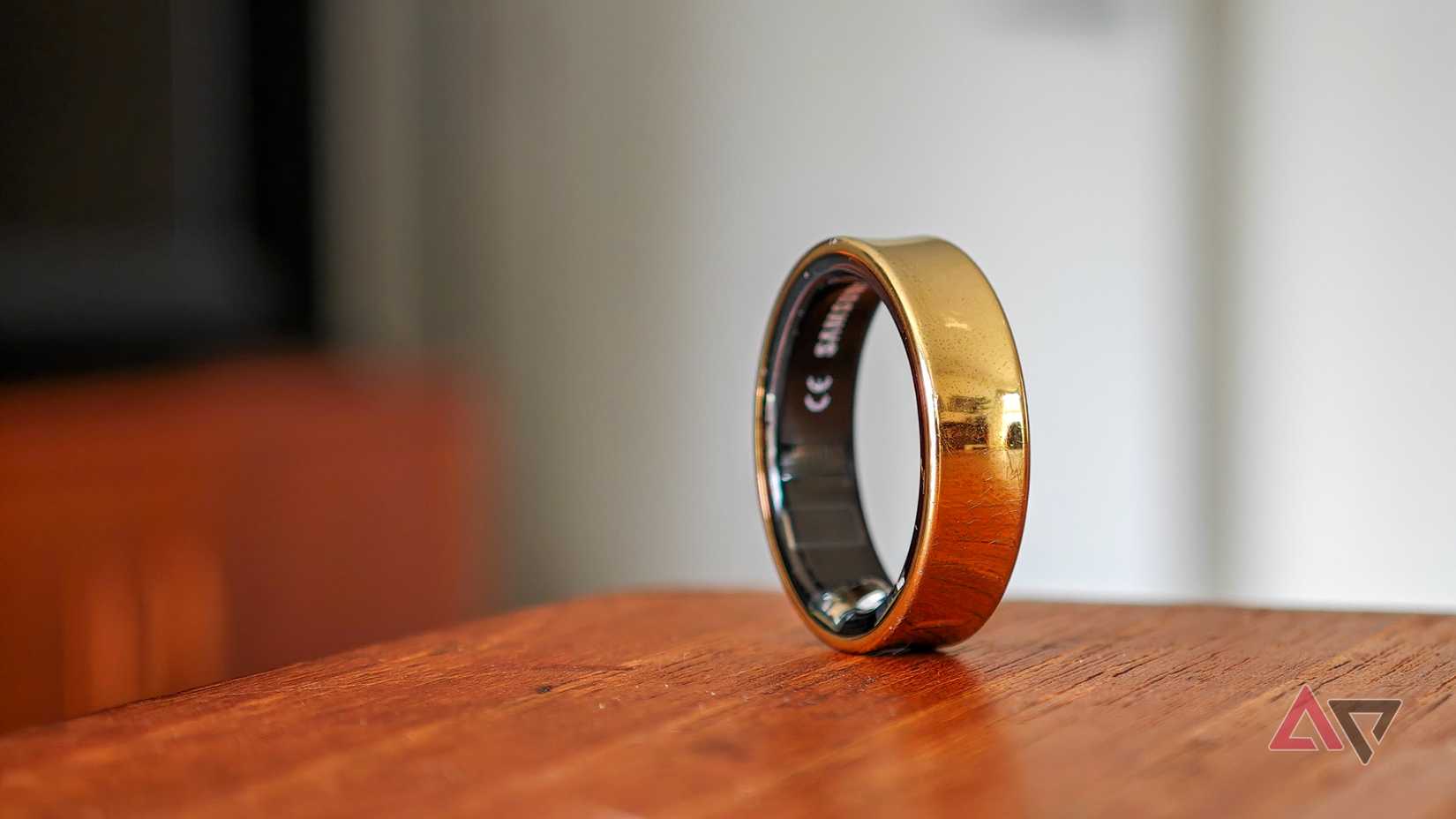 A gold Samsung Galaxy Ring resting vertically on the edge of a wooden table