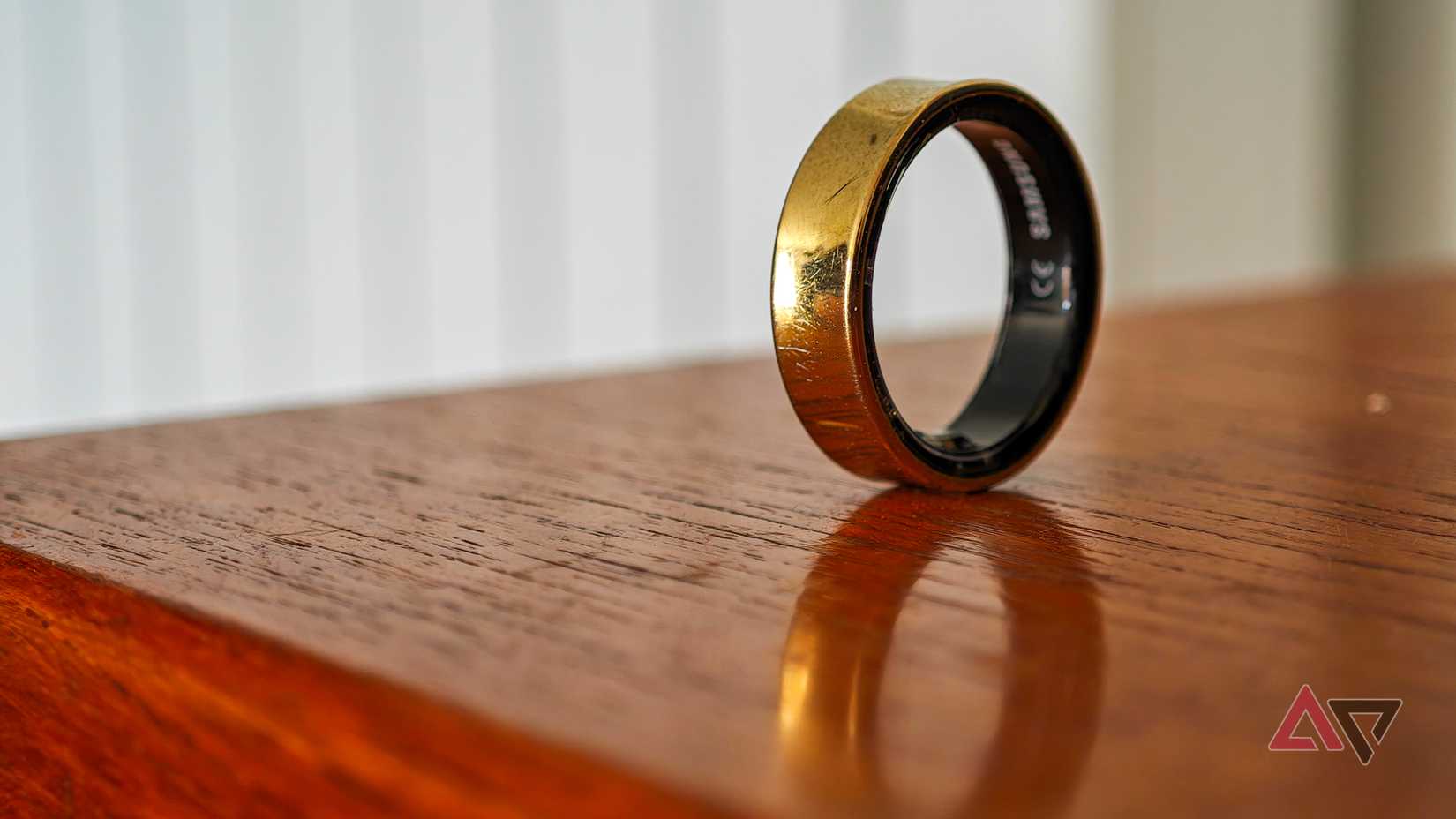 Um Samsung Galaxy Ring dourado apoiado na borda sobre uma superfície de madeira
