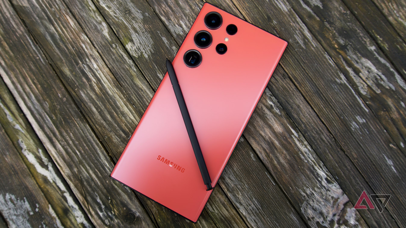 Uma foto de um Galaxy S23 Ultra vermelho voltado para baixo em uma superfície de madeira com a S Pen em cima