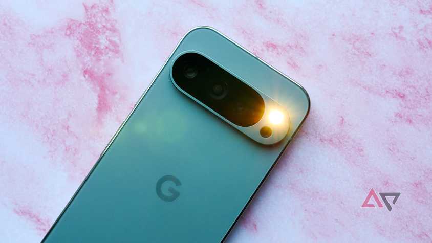 A Pixel 9 Pro with the flashlight turned on against a pink backdrop