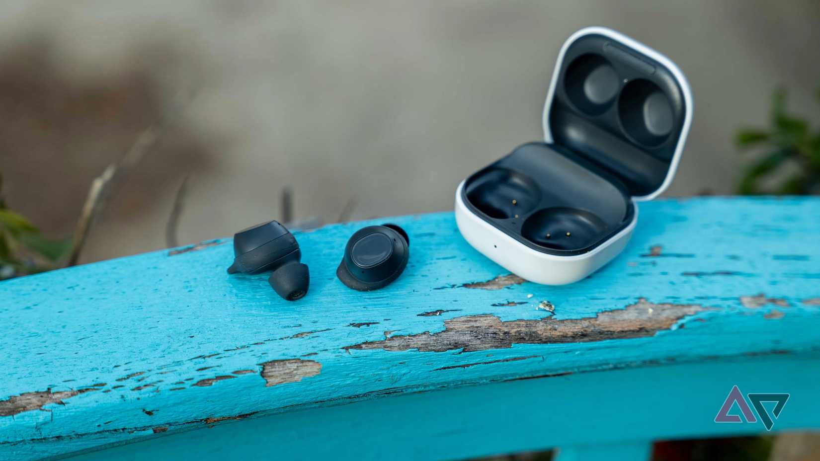 The Galaxy Buds FE out of the open case on a blue rail