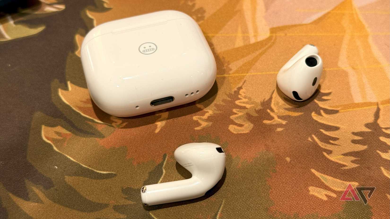 Apple's AirPods 4 charging case and earpods on a forest-stye backdrop