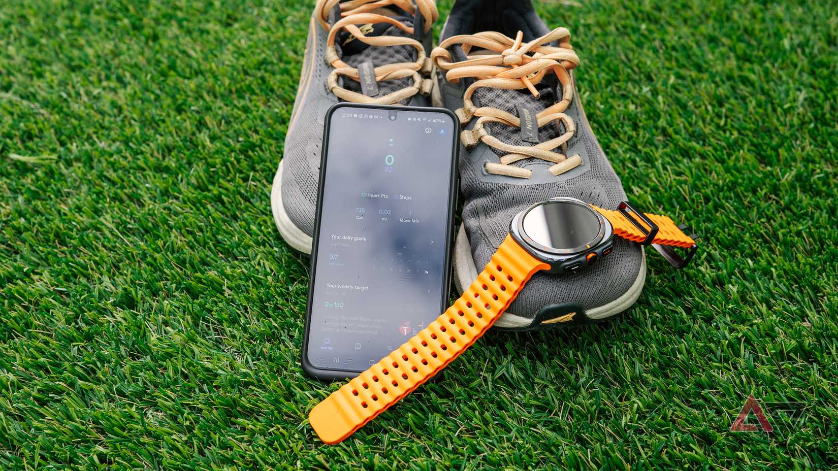 Um Samsung Galaxy S22 com o aplicativo Google Fit na tela apoia-se em um par de tênis de corrida ao lado do Samsung Galaxy Watch Ultra.