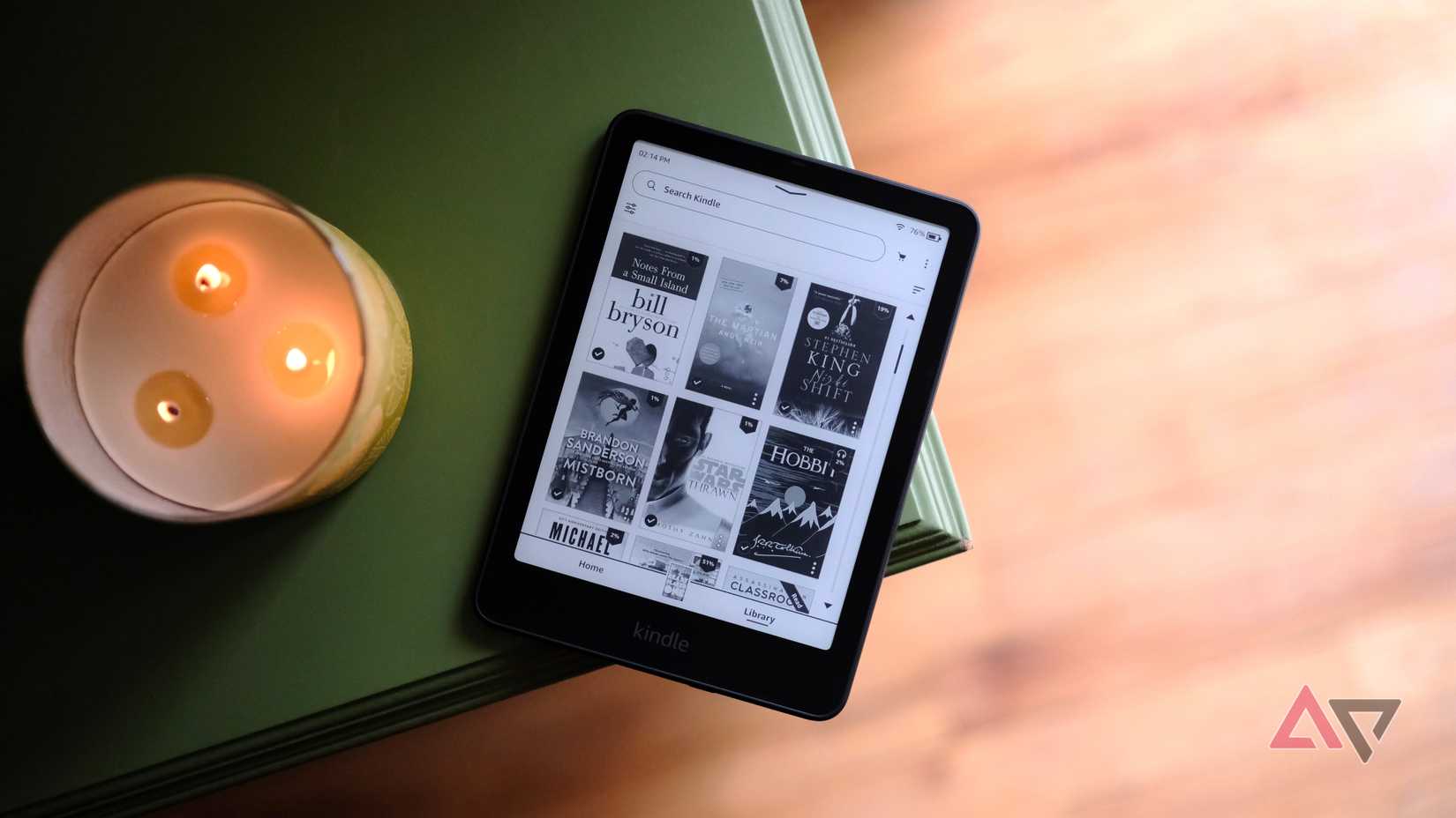 Kindle Paperwhite (2024) deitado na borda da mesa mostrando uma tela com seleção de livros
